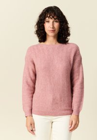 Rosa sweater med fiskbensmönster, rund halsringning och långa ärmar, tillverkad av mjukt texturerat material, tillsammans med vita byxor.