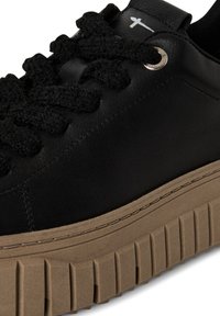 Schwarzer Ledersneaker mit dicken, strukturierten schwarzen Schnürsenkeln und einer beigen Gummisohle mit tiefen Rillen und Nahtdetails.