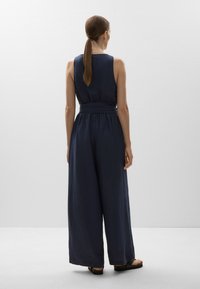 Marineblauer ärmelloser Jumpsuit mit tailliertem Gürtel und weitem Bein. Aus leichtem Stoff gefertigt, mit glatter Textur und minimalistischem Design.