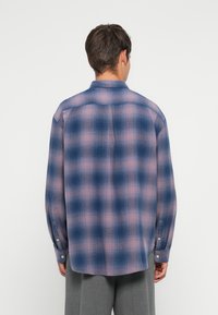 Checked flannel shirt featuring a blue and pink pattern, long sleeves, a folded collar, and buttoned cuffs. Soft texture and relaxed fit.