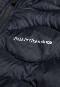 Námornícky izolovaný sveter s prešívanou textúrou. Na prednej strane je diskrétne strieborné logo "PeakPerformance", ktoré zdôrazňuje jeho športový dizajn.