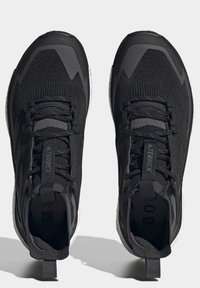 Schwarze Sportschuhe mit einem strukturierten Strickobermaterial, verstärkter Zehenkappe und kontrastierender weißer Sohle. Mit Schnürsenkeln und einer Zuglasche an der Ferse.