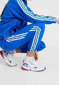 Chándal azul con rayas verticales blancas y pantalones a juego; zapatillas blancas con acentos en rosa y azul, detalles grises y cordones.
