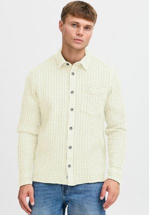 Light beige textured shirt with a button-up design, two chest pockets, round collar, and grey buttons. Long sleeves with cuffs.