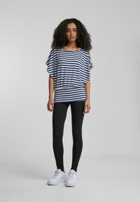 Haut à rayures à manches courtes en bleu marine et blanc, coupe ample, taille cintrée. Associé à des leggings noirs et des baskets blanches, sur un fond uni.