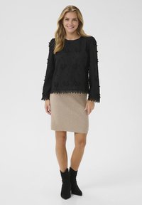 Sort langærmet bluse med blomstermønster og blonder, parret med en beige striknederdel og sorte ruskinds ankelstøvler.