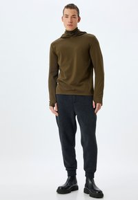 Sudadera de manga larga en verde oliva con cuello alto, combinada con pantalones de chándal de forro polar en gris oscuro y botas gruesas negras. Textura suave, diseño ceñido.