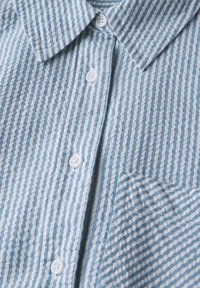 Camicia button-up a righe blu chiaro e bianche realizzata in tessuto texture, con colletto classico e taschino sul petto. Bottoni bianchi.