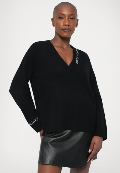 Schwarzer V-Ausschnitt-Pullover mit langen Ärmeln, ausgestattet mit weißen Textdetails am Ausschnitt und an den Bündchen, aus einem weichen, strukturierten Material gefertigt.