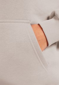 Sweatshirt gris clair avec une texture douce. Il dispose d'une poche avant et de poignets côtelés. Les coutures soigneusement cousues mettent en valeur le design.