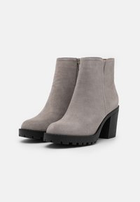 Botines de ante gris con punta redonda, cremallera lateral y un tacón grueso de goma negra. La suela presenta un dibujo texturizado para mayor agarre.