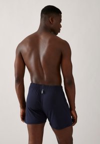 Shorts de bain bleu marine en tissu doux, dotés d'une taille élastique et d'une petite étiquette logo au dos. Design classique, longueur au-dessus du genou.