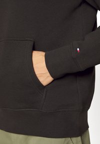 Sudadera negra hecha de suave material de algodón, con un bolsillo en el frente y puños acanalados. Incluye un pequeño logo en la manga.