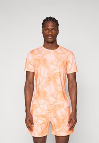 Sæt bestående af en orange mønstret atletiktrøje og shorts, der har et mesh-lignende design med en tætsiddende silhuet og rund halsudskæring.
