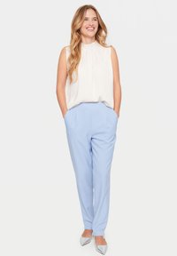 Svetle modré šité kalhoty se bočními kapsami, spárované s krémovou bezramínkovou blůzou. Stříbrné ploché boty s špičatou špičkou dotvářejí outfit.