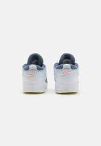 Heledad sinine ja tume sinine sneaker, millel on valge tald, roosa Nike logo kanna juures ja tekstureeritud, pehme kangas ülemine osa.