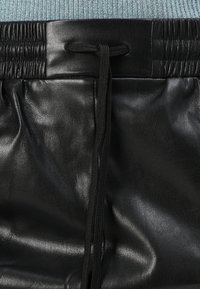 Zwarte faux leren broek met een elastische tailleband en koordje. Glad, matte textuur met geplooide details in de taille.
