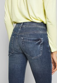 Snygga mörkblå jeans i denim med medelhög midja, bakfickor och lätt blekning, tillsammans med en ljusgul långärmad topp.