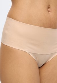 Tronc de femme portant des sous-vêtements taille haute couleur nude, sans coutures, en tissu lisse et sans ornements visibles.