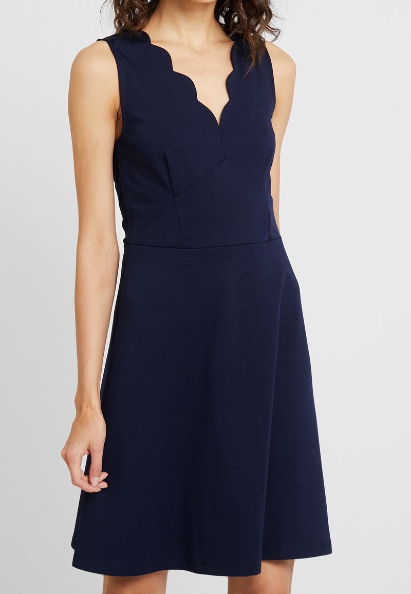Marinblå ärmlös klänning med en scalloped halsringning, åtsittande bodice och en utsvängd A-linje kjol, gjord av mjukt, stretchigt material.