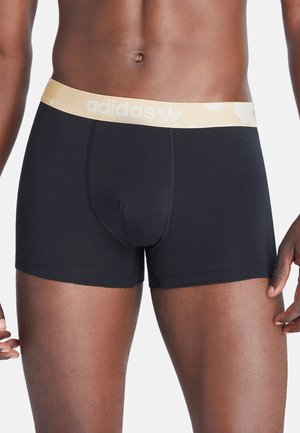 Caleçons boxers noirs avec une coupe ajustée, dotés d'une taille élastique beige clair portant le logo adidas en blanc. Tissu lisse.