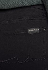 Black denim pants with a standard fit, featuring a subtle wave pattern in dark stitching and a fabric label with the text "for all man kind."
