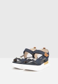 Sandali platform in denim con cinturini regolabili, decorati con accenti metallici, suole in gomma bianca e una linguetta del tallone rinforzata in tonalità marrone.