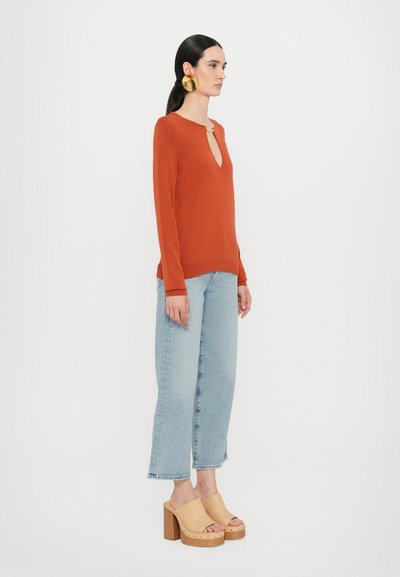 Burnt orange long-sleeve sweater with a deep V-neck, paired with light blue wide-leg jeans and tan platform clogs with a wooden sole.
