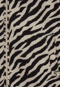 Čiernobiela tkanina s potlačou zebry, ktorá obsahuje zips, nášivkovú vrecko so zapínaním na gombík a štítok s nápisom "posielam ti lásku" v zlatej farbe.