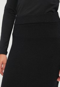 Svart strikket blyantskjørt med ribbestrikket midje. Glatt tekstur med en tettsittende fasong som slutter under kneet. Ingen synlige mønstre eller detaljer.