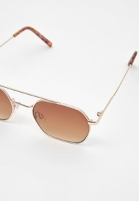 Ochelari de soare cu ramă aurie, dotati cu lentile ovale de culoare brown gradient. Perițe de nas din cauciuc transparent și brațe din tortoiseshell maro. Finisaj lucios, design ușor.
