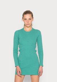 Vestido ajustado de mangas longas em tecido canelado turquesa, com um detalhe de costura ondulada na zona do busto e um corte curto, acima do joelho.