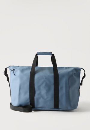 Bolsa de deporte grande azul con asas negras y correa ajustable para el hombro sobre un fondo liso y claro.