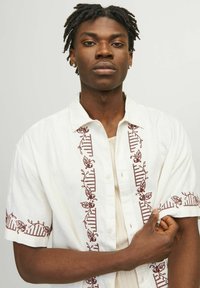 Hvid kortærmet skjorte med maroon blomsterbroderi langs knaplinjen og ærmerne; blød tekstur, afslappet pasform og knaplukning.