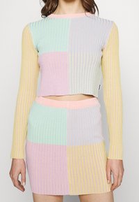 Geribbelde breisels co-ord set met een cropped top en een aansluitende rok in pasteltinten: mintgroen, roze, lavendel en geel. Lange mouwen.