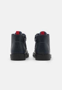 Mörkblå läderstövlar med en slät yta, röda tygmärken bak, och svarta gummisulor. Har dragkedja på sidan.