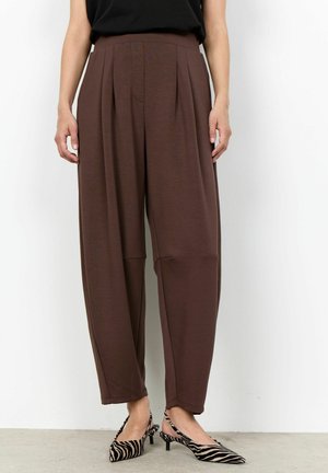 Personne portant un pantalon marron ample taille haute avec des plis, assorti à des chaussures à bride arrière à talon kitten à imprimé zèbre noir et blanc.