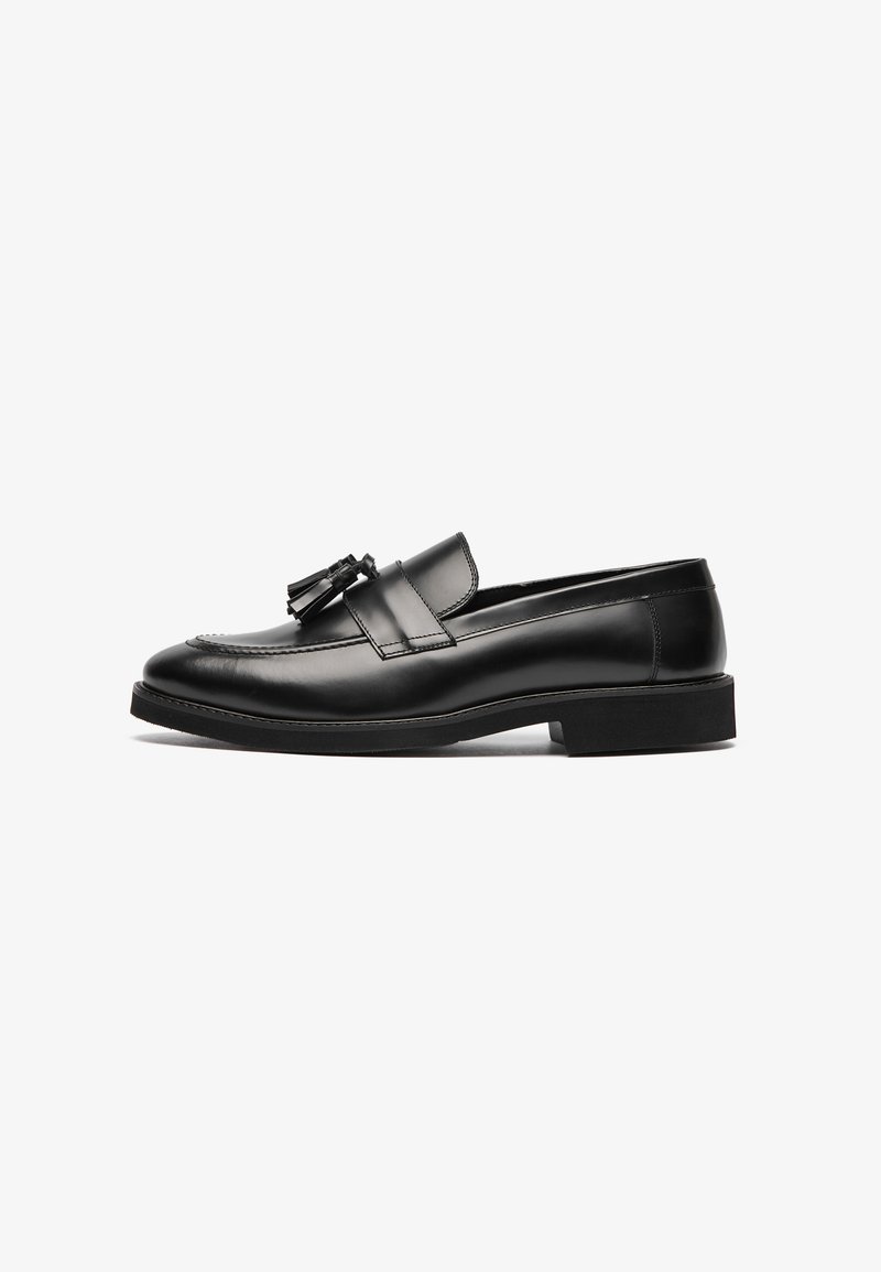 Mocassins en cuir noir avec une surface lisse, un bout arrondi et un gland décoratif sur la bride. Semelle plate et détails de couture subtils.