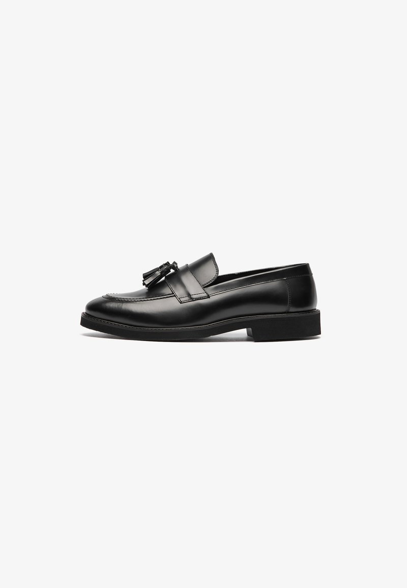 Black leather loafers with a smooth surface, a rounded toe, and a decorative tassel on the strap. Flat sole and subtle stitching detail.