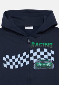 Tengerészeti zipzáras kapucnis pulóver versenyautó grafikával, zöld felirattal és világoskék kockás zászló mintával a mellkason.