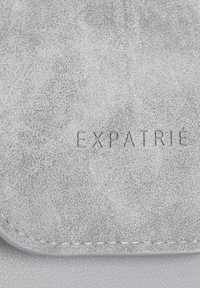 Pelle sintetica grigia con una finitura testurizzata e bordo cucito. Presenta il logo inciso "EXPATRIÉ" al centro.