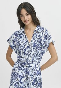 Rochie cambrată cu butoni, în albastru deschis, cu modele spirale în albastru închis. Mâneci scurte, guler și detaliu cu talie legată.