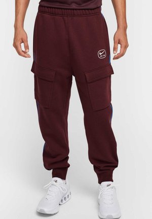 Pantaloni cargo Nike bordeaux con strisce laterali blu, vita elasticizzata e doppie tasche frontali. Realizzati in un tessuto morbido e resistente.