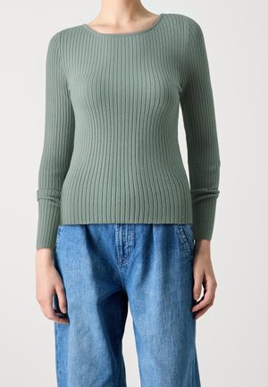 Groene geribbelde trui met een ronde halslijn en lange mouwen, gecombineerd met losse blauwe denimbroeken. Heeft een textuurstof en een aangesloten silhouet.