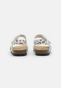 Hvite sandaler med et mønstret innvendig design med fargerike tegneserieillustrasjoner, en korkfotseng og justerbare stropper for en sikker passform.