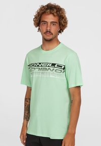Camiseta de manga corta en verde menta, hecha de tela suave, con un atrevido logo en negro y plata en el pecho y un ajuste relajado.