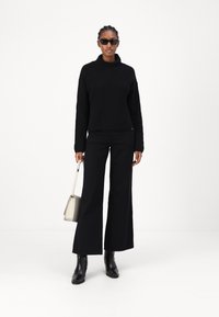 Maglione a collo alto nero a coste, abbinato a pantaloni neri svasati, stivaletti neri e una borsa crema chiara. Gli occhiali da sole completano il look.