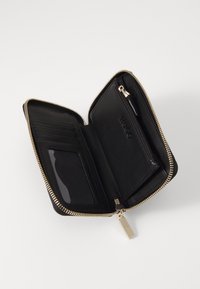 Cartera de cuero negro con cremallera en tono dorado. Cuenta con compartimentos para tarjetas, una ranura transparente para identificación y un bolsillo con cremallera para monedas. Textura suave, con un branding minimalista.