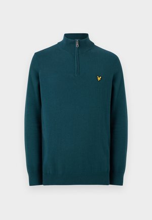 Türkiz hosszú ujjú, negyedig cipzáros pulóver magas gallérral és kis sárga madár logóval a bal mellrészen.