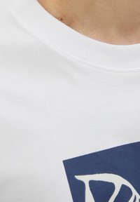 Hvid bomulds t-shirt med rund hals, der har et mørkeblåt grafisk design med vinkelformede figurer og tekst i lys farve nær halsen.